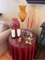 Table setup showing amber vase, pink vase, clear crystal candle holders with red candles, brass candle holders, white pillar candles on black holders, and small brass decor objects.