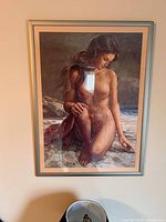 Framed print of a nude woman sitting on a beach, hung on a wall, in a silver frame with matting and glass front