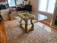 Full view of rectangular glass top dining table with carved wood pedestal base in a living room setting