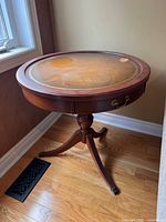 Full view of the round vintage wooden accent table with leather top showing surface wear and marks.