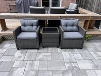 Front view of both wicker armchairs flanking side table on stone patio