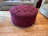 Full view of round red tufted ottoman on casters in living room.