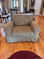 Front view of large green patterned upholstered armchair showing full shape and cushion details in a dining room setting