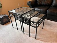 Set of 3 glass nesting tables showing the clear glass tops and black metal scrollwork frames, nested together