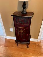 View of red floral hand-painted accent cabinet showing drawer and door detail