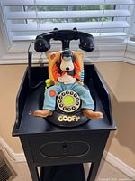 Front view of vintage Telemania Disney Goofy Telephone showing Goofy seated with rotary dial and handset on his head.