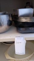 Metal mixing bowls and various baking sheets and pans stacked in a shelf