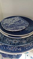 Stack of five blue and white ceramic plates with different floral and scenic transferware designs.