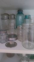 Nine assorted canning jars on shelf, some with wire locking lids, some with metal lids, including one blue-green glass jar