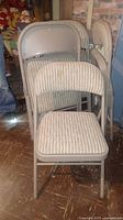 Four beige metal folding chairs with ribbed textured upholstery on seats and backs, stacked together.