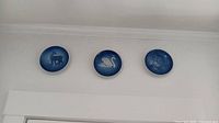 Three blue decorative plates mounted on a white wall featuring animal and bird designs.
