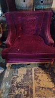 Front view of a vintage burgundy velvet upholstered armchair with visible wear and a small tear on the seat cushion, showing the plush texture and mid-century style shape.