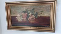 Framed painting showing three roses on wooden table with muted background, encased in an ornate gold tone wood frame