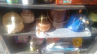 Photo showing various tea pots including ceramic and metal, and a blue watering can along with some other miscellaneous items.
