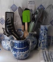 Vintage blue and white ceramic holders filled with various kitchen utensils arranged on countertop with matching tile backsplash