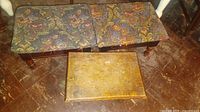 Photo showing two rectangular footstools with vibrant floral fabric tops and one smaller wooden footstool, all vintage with signs of wear.