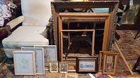 Several framed artworks and empty wooden frames arranged on the floor and leaning against an armchair.