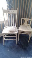 Two vintage white painted wooden chairs placed next to each other on blue carpet showing general look and color.