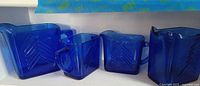 Front angle of four cobalt blue glass pieces on shelf showing square shape and chevron patterns