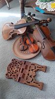 Four violins including full size and miniature displayed on floor with wooden plate