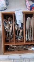 Top view of silverplate flatware pieces arranged in a wooden tray including spoons, forks, and knives.