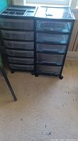 Two black plastic storage units on wheels with multiple drawers for organizing, shown standing on floor.