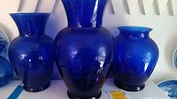 Photo showing three blue glass vases of different sizes and shapes on a shelf.