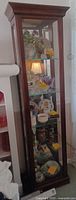 Full view of the tall wood and glass display cabinet containing various decorative items inside, showing glass door and shelves.