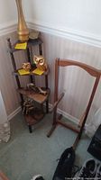 Photo showing small corner shelf with three tiers holding small brass animal figurines, folding valet stand nearby.