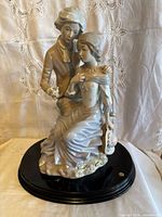 Front view of porcelain figurine couple seated on black base, showing detailed period clothing and floral accents.