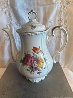 Front view showing colorful floral decoration and gold trim on lid, handle, and spout of porcelain teapot.