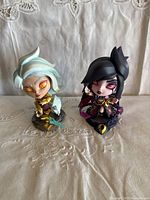 Front view of two League of Legends vinyl figures placed side by side on fabric background, showing detailed face and torso features.