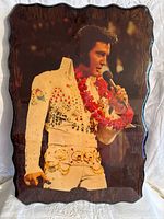 Front view of lacquered wooden plaque showing Elvis Presley in white rhinestone jumpsuit and red lei, holding microphone.