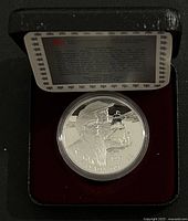Open black presentation case with silver proof coin and certificate inside.