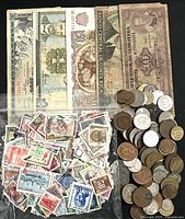 Photo showing 5 assorted foreign paper banknotes, around 75 coins, and about 100 assorted postage stamps scattered on a black background.
