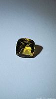 Close-up photo of natural golden citrine gemstone, cushion cut shape, showing facets and golden yellow color.