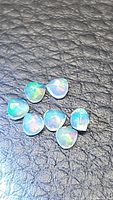 Seven natural Ethiopian opals faceted as pear teardrop shapes exhibiting multicolored flash on black textured background