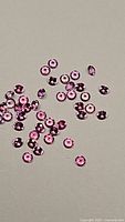 Close-up photo of numerous small round pink sapphire gemstones scattered on a flat surface, showing calibrated size and color.