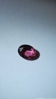 Oval cut natural rhodolite garnet gemstone photographed on a flat surface, showing deep pink purple color and clarity.