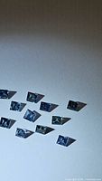 Photo showing 11 square cut blue sapphire gemstones spread on a flat surface under light to highlight their luster and clarity.