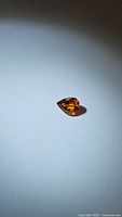 Photo showing pear-shaped natural spessartite garnet gemstone with deep orange color and reflective facets on white background.