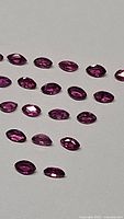 Top view of multiple marquis cut untreated ruby gemstones arranged in rows on a white surface.
