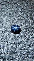 Oval cabochon cut natural blue star sapphire against textured dark background showing distinct 6-ray star pattern under light.