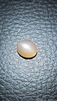 Photo shows the oval peach moonstone cabochon gemstone on textured black surface, highlighting its smooth cabochon shape and peach color.