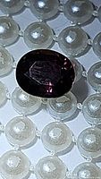Natural oval cut sapphire showing purple to deep fuchsia pink purple color change on pearl background.