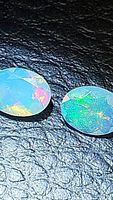 Close-up image of two natural oval cut Ethiopian opals showing their play-of-color on a dark textured surface.