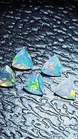 Close-up photo showing five triangular faceted opal gemstones with visible iridescent colors against a textured black background.