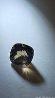 Photo of natural fancy checkerboard cut smoky quartz gemstone showing cushion-shaped stone with light reflections on a plain surface.