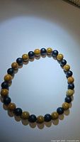 Bracelet laid out in a circle showing alternating black onyx and wood grain jasper beads in good lighting.