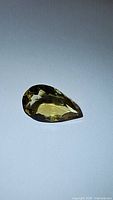 Photo of a natural golden citrine gemstone cut into a pear shape with faceted surface showing color and clarity.